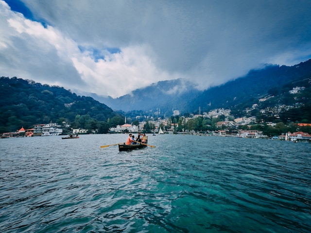 people enjoying boatride in blue water of Naini lake with cloud covered Mountains at the back