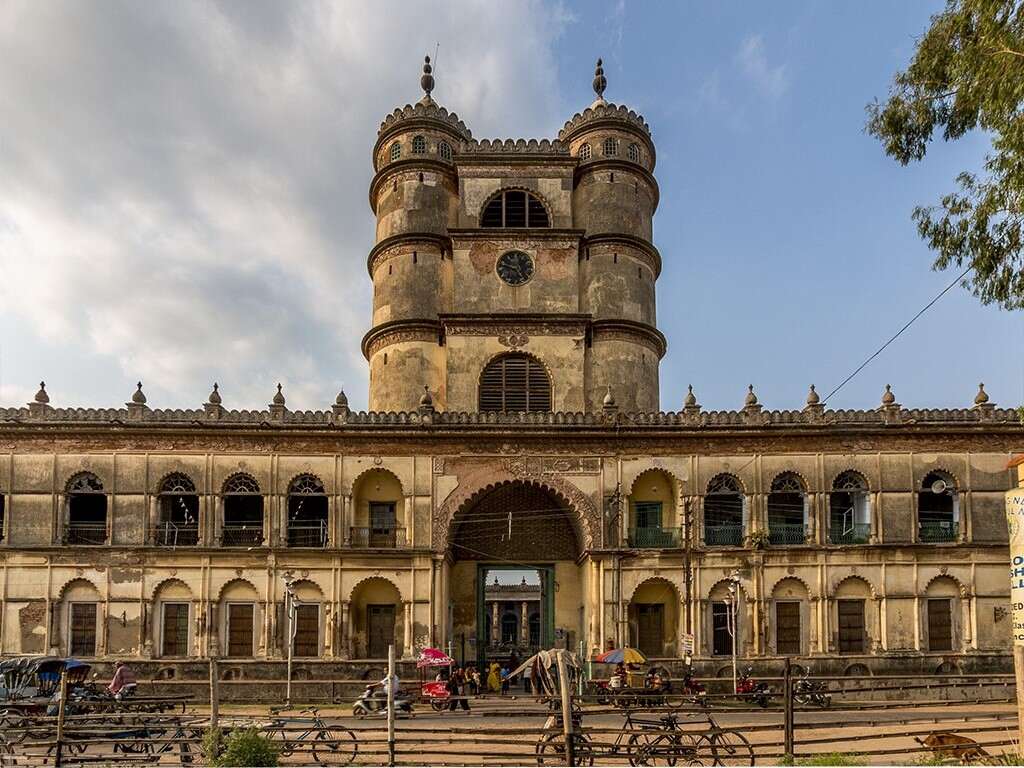 An old mosque with clock tower and stairs with people around.