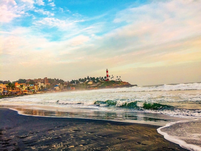 Scenic beach with waves crashing and a lighthouse in the background.