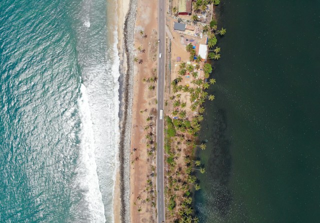 Aerial view of sandy beach meeting turquoise ocean waters under clear blue sky.