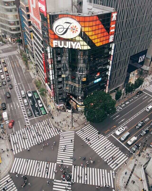 A bustling Tokyo intersection with cars, pedestrians, and tall buildings in the background.