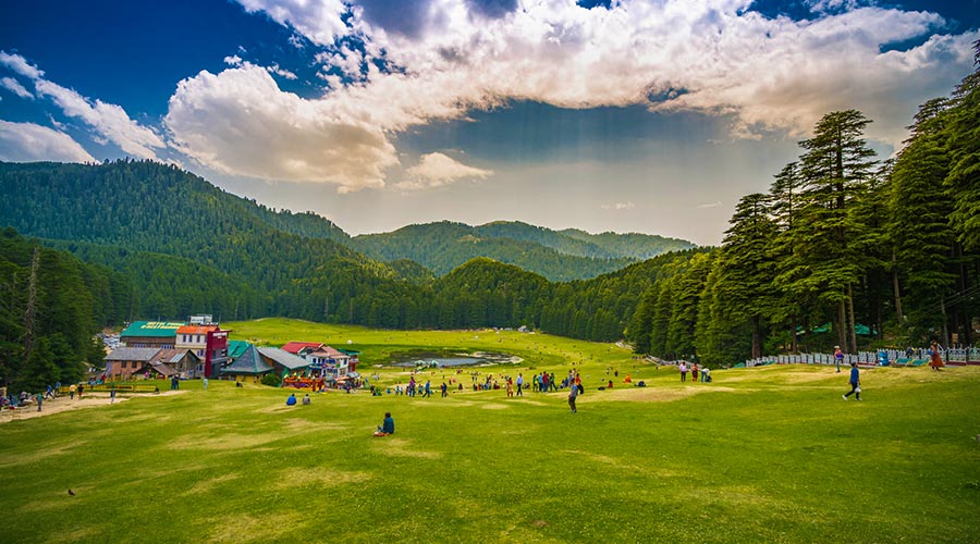 Group of people walking in a vibrant green field with towering mountains in the distance