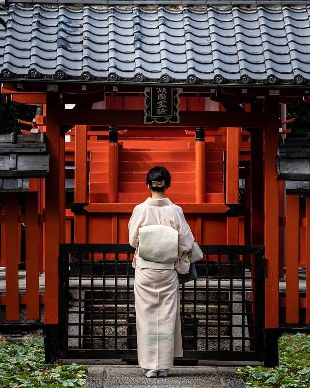 A woman in white attire approaching a red building.