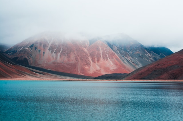 Beautiful lake in front of pink and blue colour mountains covered with clouds.