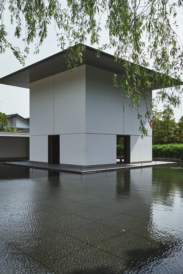 Scenic view of a small white building next to a tranquil pond in a serene setting.