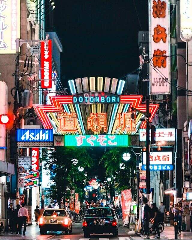 Dotonbori street at night, filled with colorful neon signs and bustling cars.