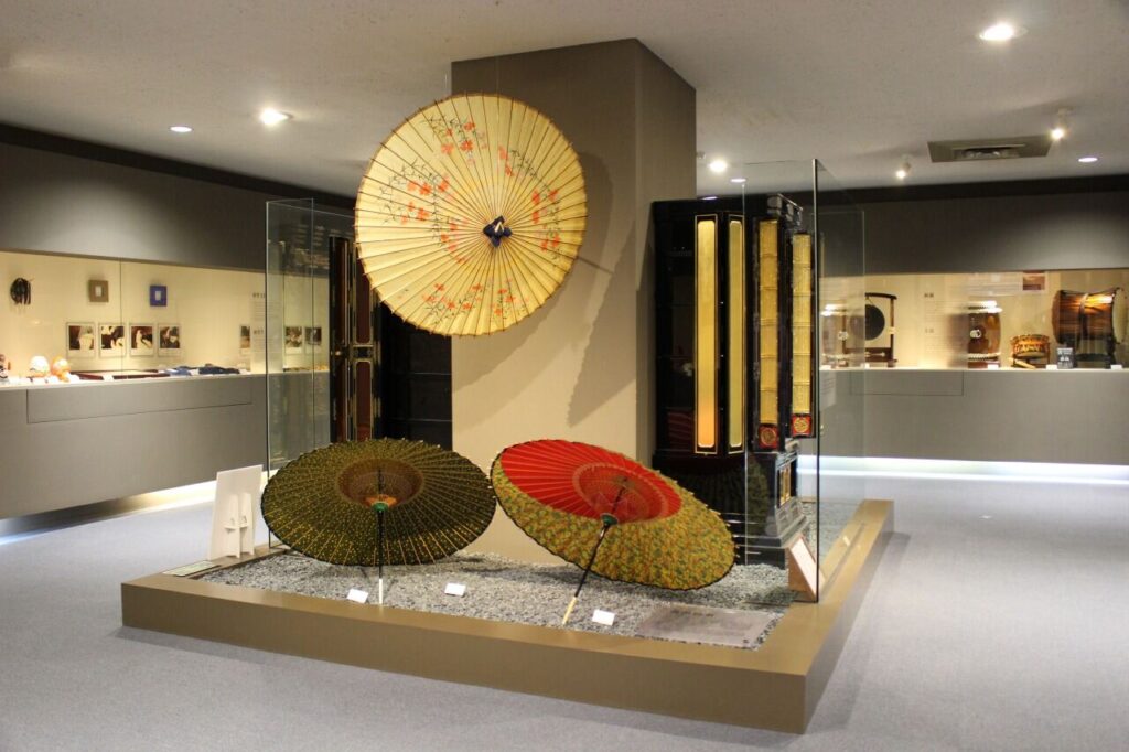 Several colorful Asian umbrellas on display in a glass case in art museum at kanazawa