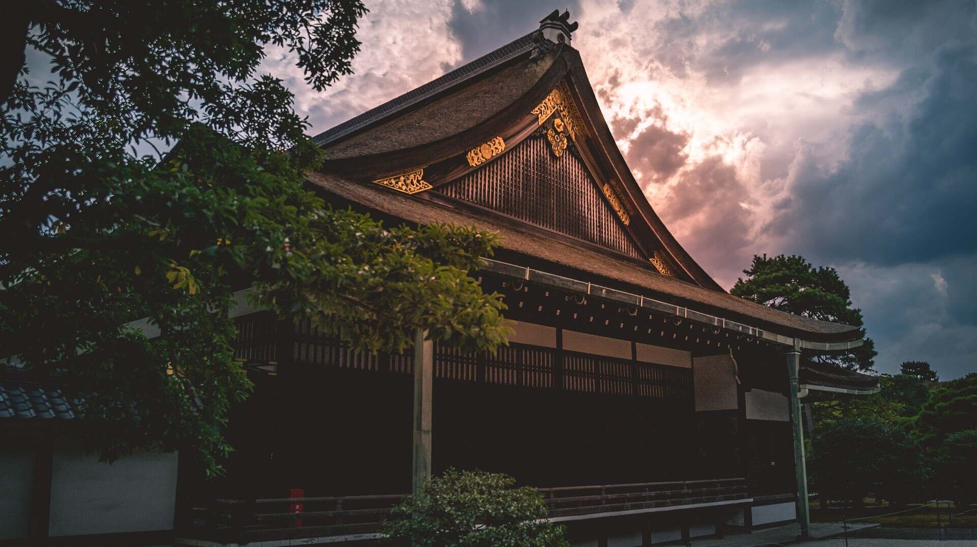 A serene Japanese temple surrounded by lush greenery, set against a backdrop of a cloudy sky.