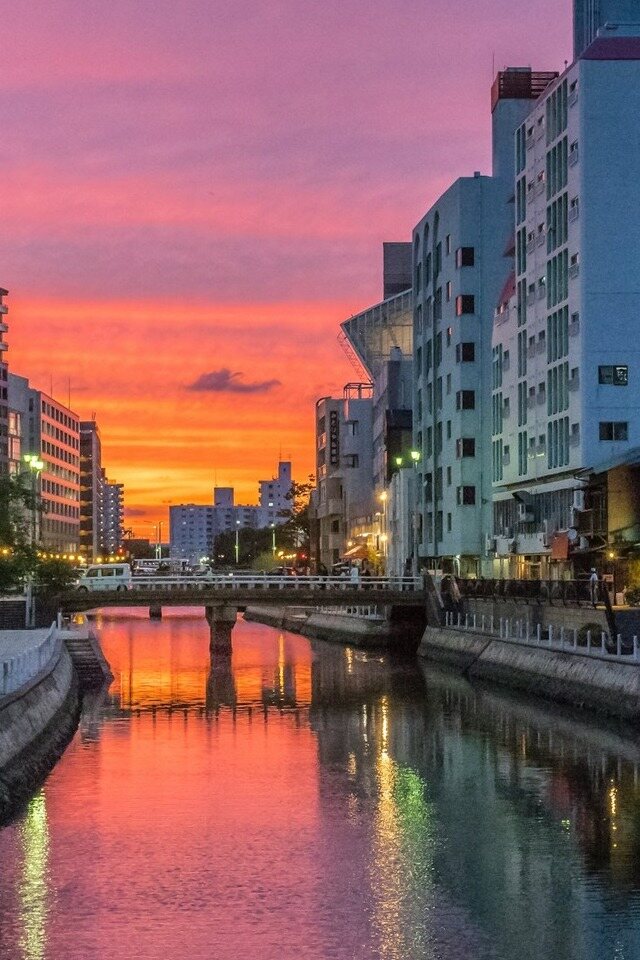 Urban river with buildings under a colorful sky.