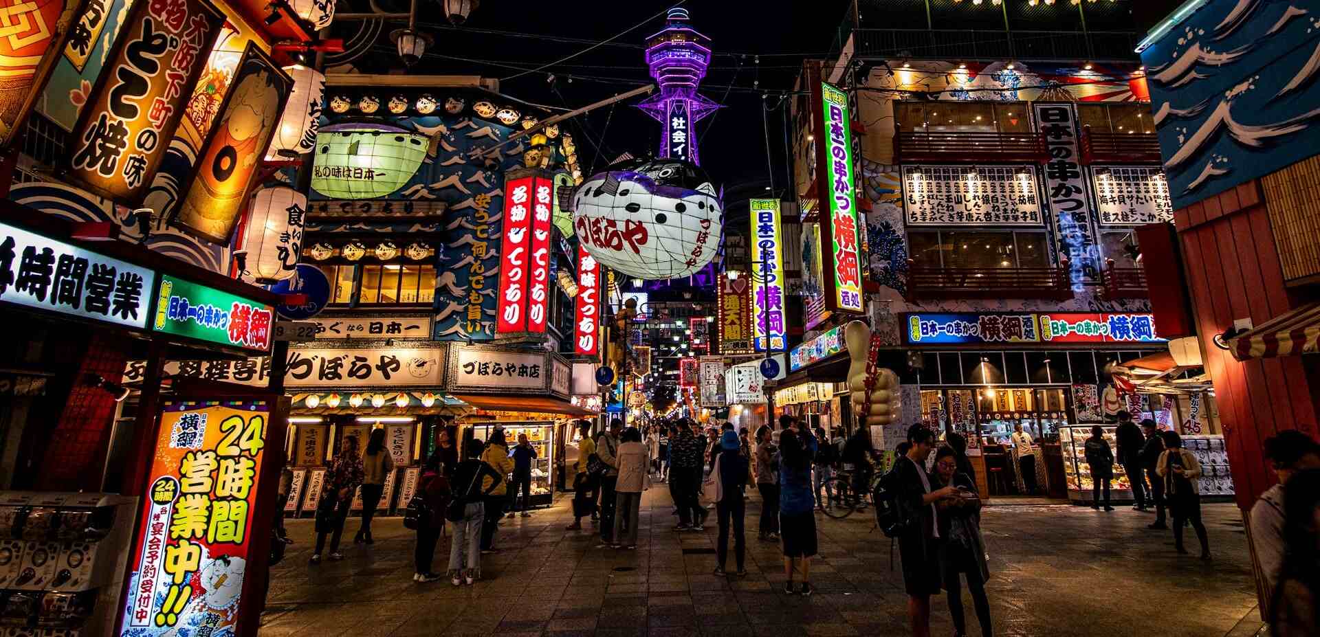 A bustling city street at night illuminated by colorful neon signs.