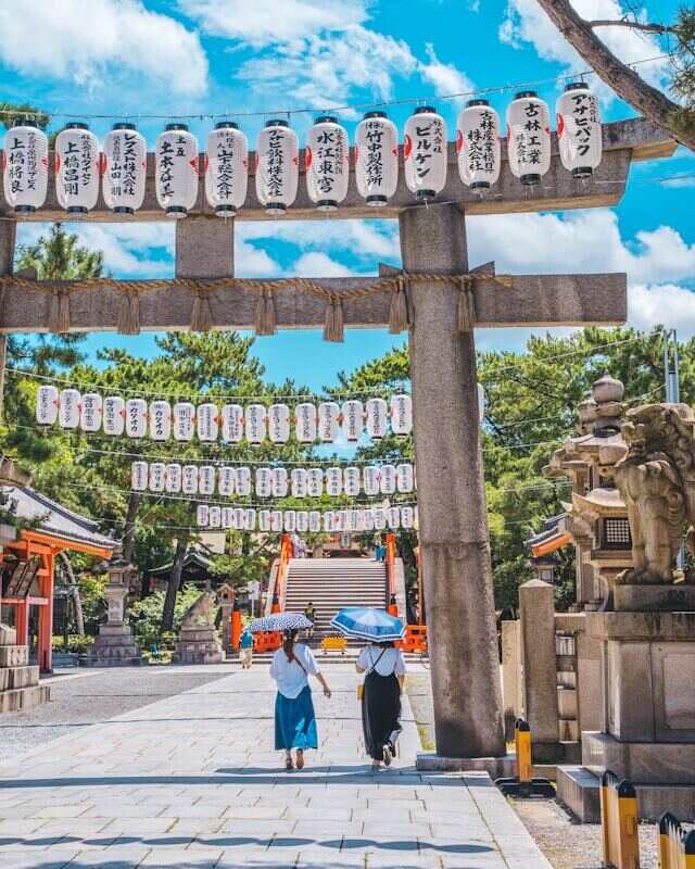 Two women walking under a "Shinto Shrine" archway, symbolizing their visit to the sacred place.