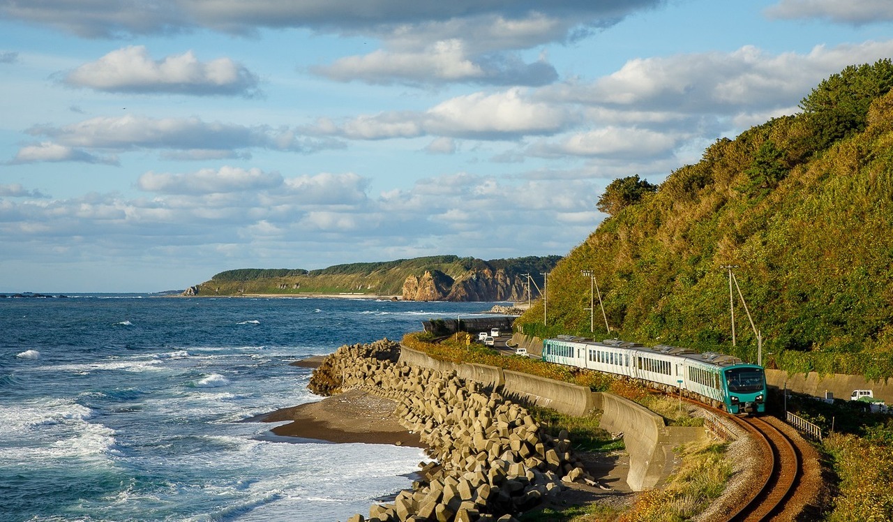 A train moving along the tracks by the ocean, with waves crashing in the background.