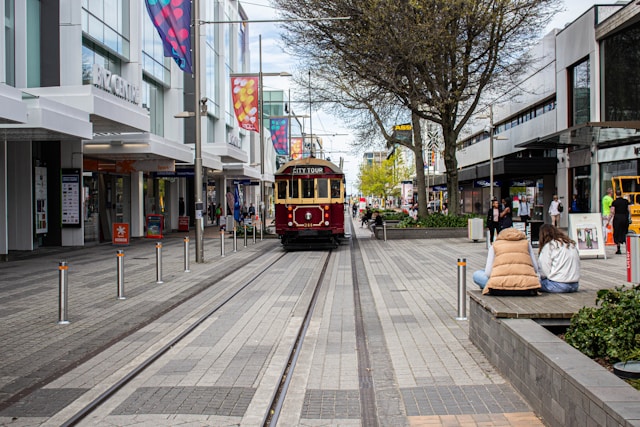 A vintage trolley car moving along a city street, surrounded by buildings and pedestrians.