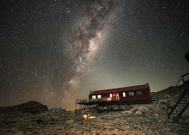 The Milky Way shining brightly over a mountain hut, creating a stunning night sky view.