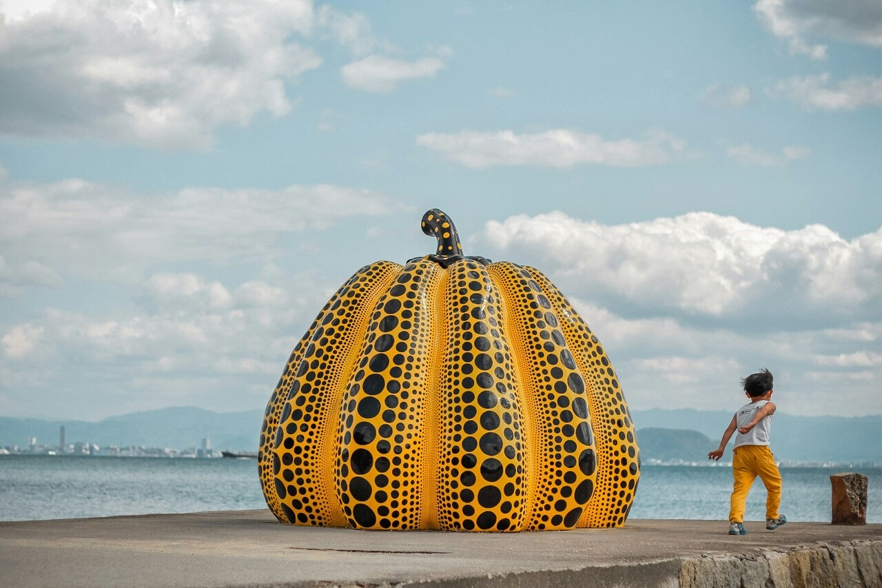 A child standing next to a large yellow pumpkin in a pumpkin patch.