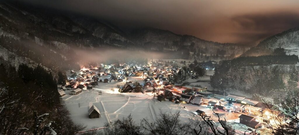 A picturesque snowy village at night, illuminated by twinkling lights, creating a cozy and enchanting atmosphere.