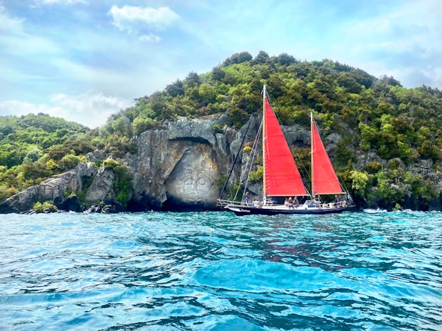 A sailboat with vibrant red sails gracefully glides across the vast expanse of the ocean.