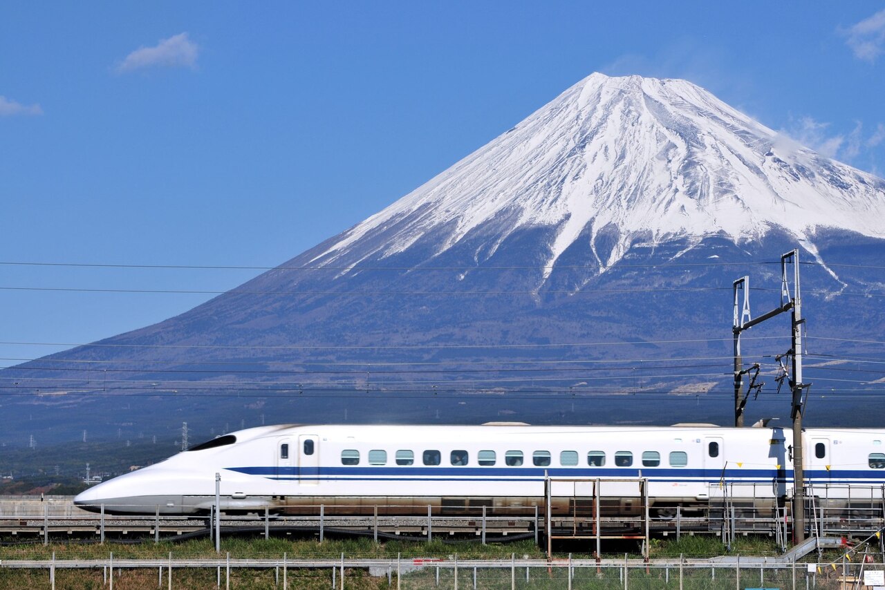 A white and blue train traveling on the tracks with Mt Fuji in the background.