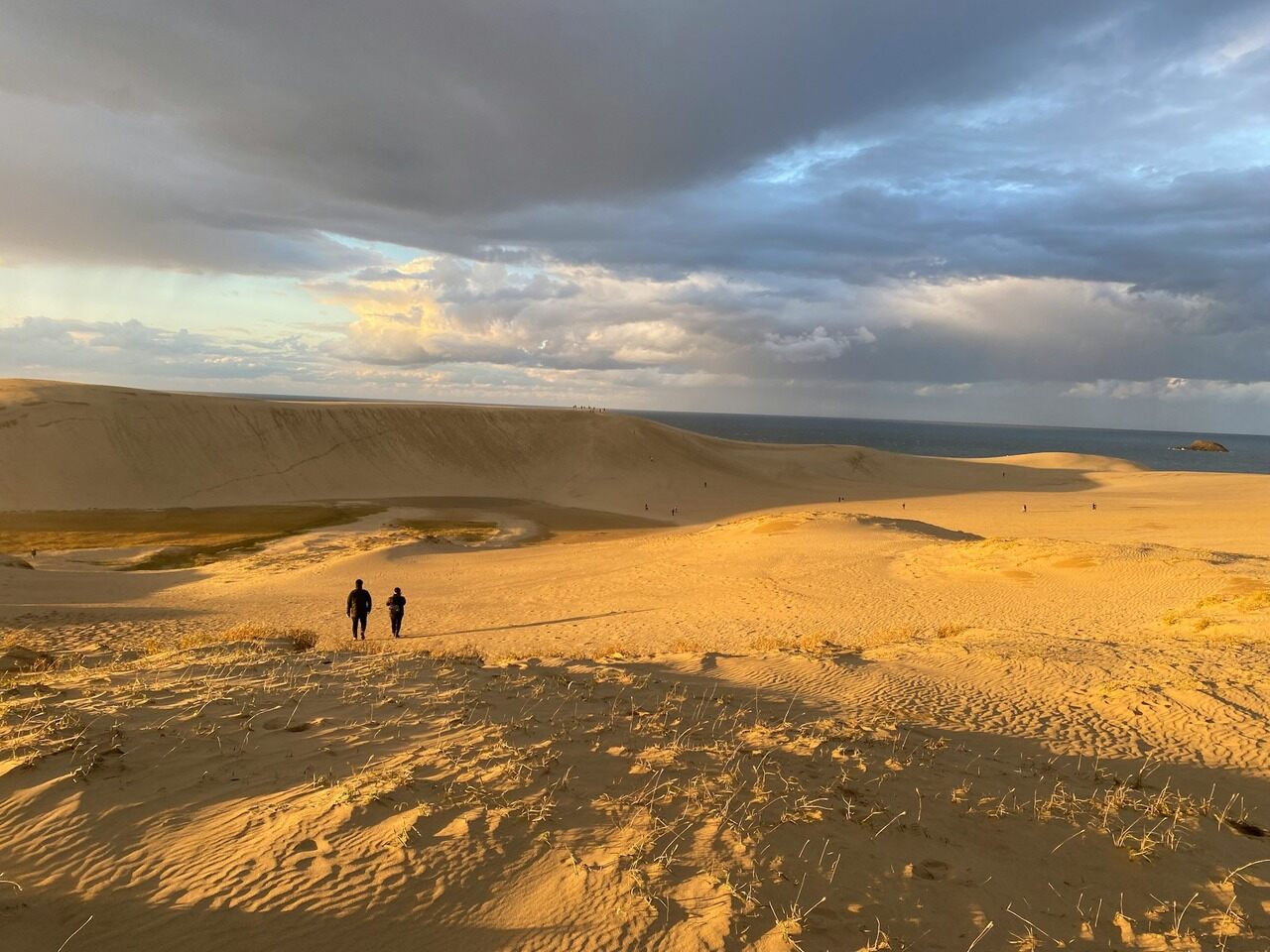 Two individuals strolling on sandy dunes during sunset, creating a picturesque scene.