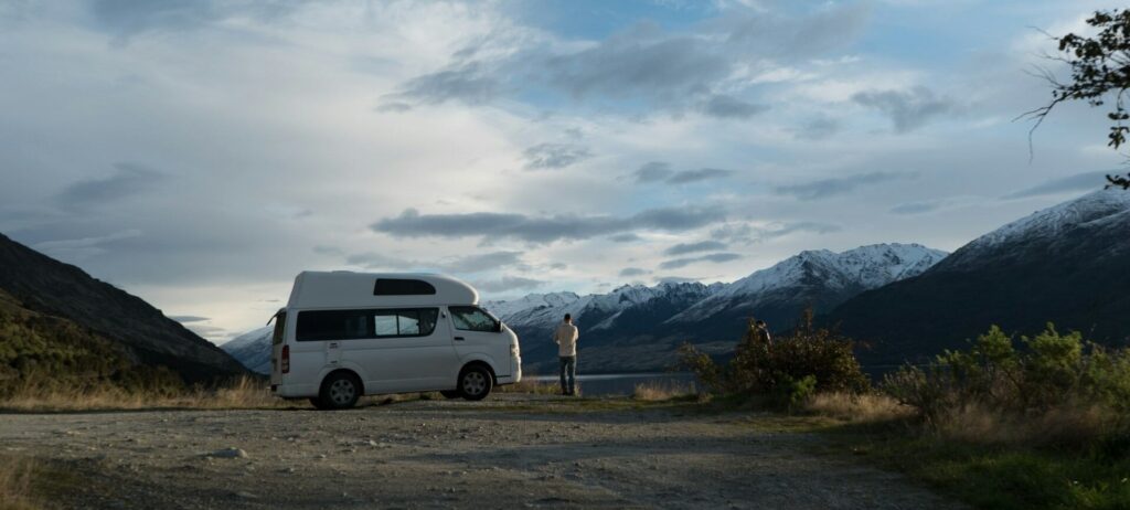 Person standing next to a white Van with Mountains in the background