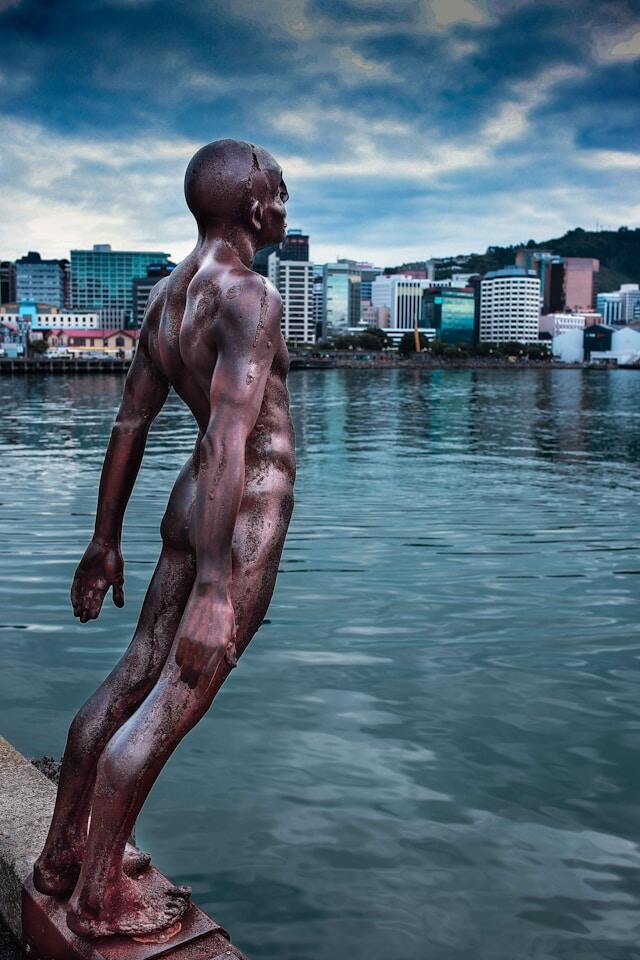 A statue of a man standing on a dock by the water.